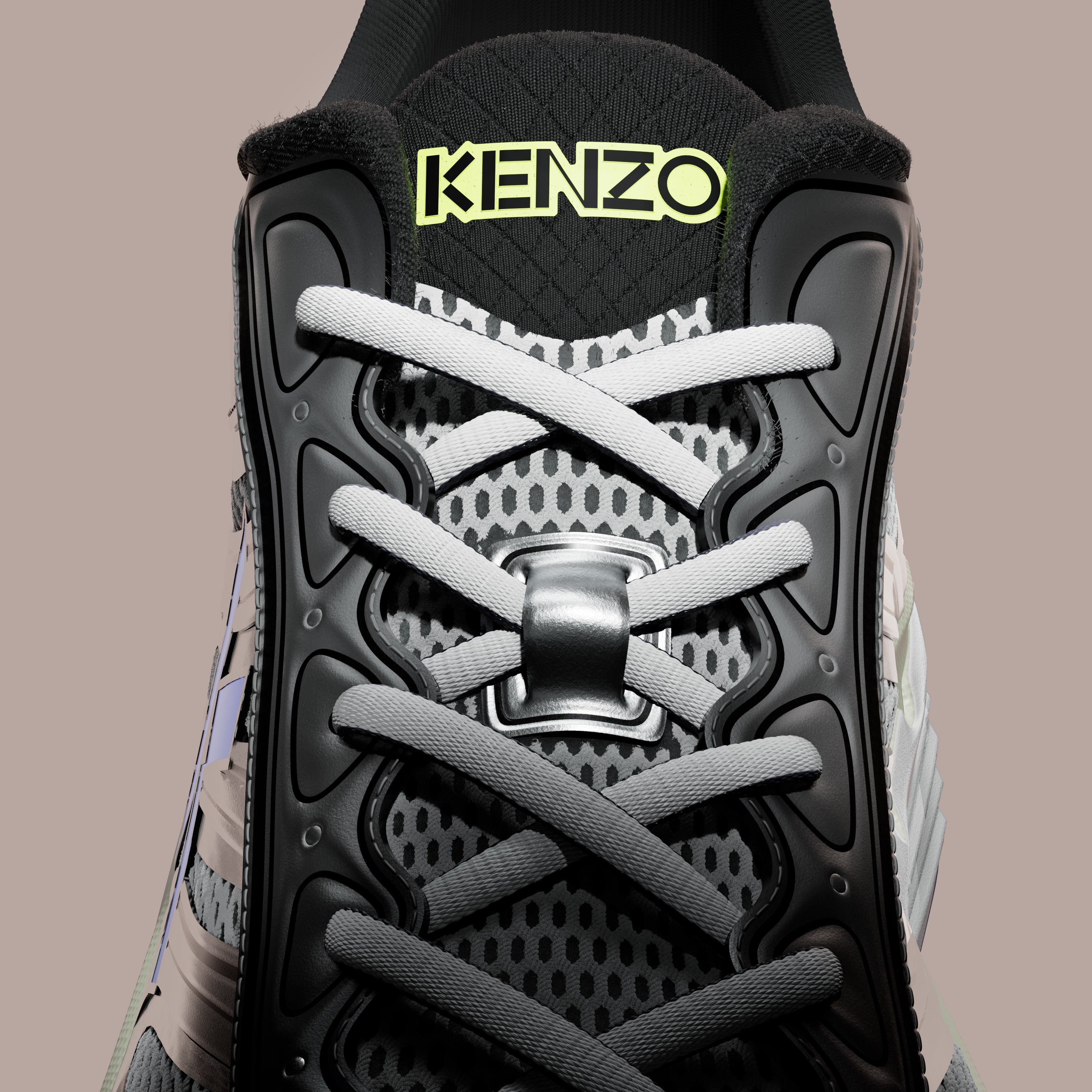 Top view of the shoe's laces crossing over grey mesh, with a black tongue printed with KENZO in neon yellow.