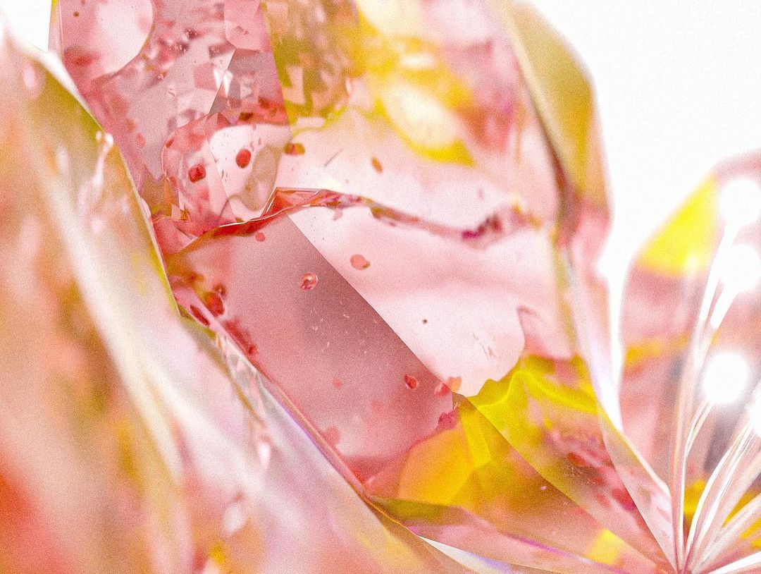 Extreme close-up of crystalline pink and yellow petals, faceted and translucent, with small flecks suspended inside.