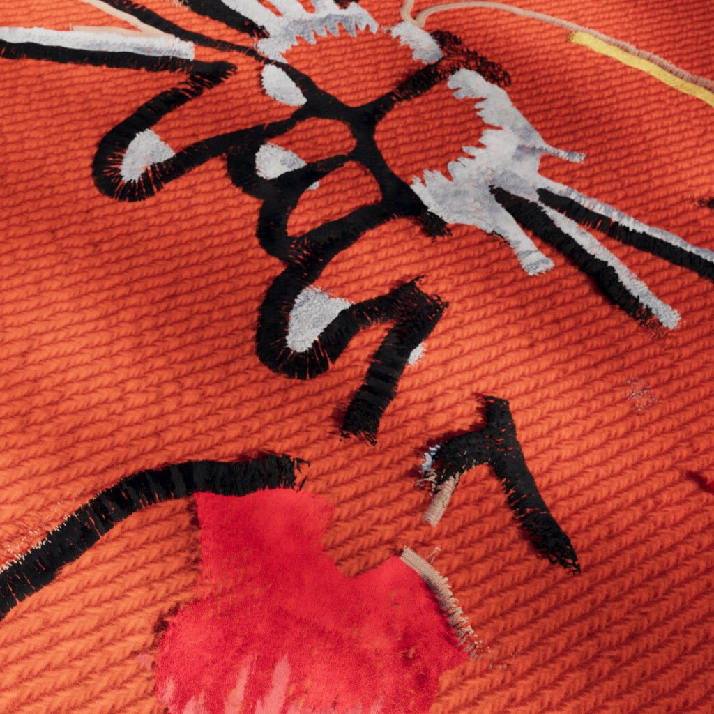 Close-up of orange ribbed knit with black and white stitched strokes, a thin yellow line and a patch of red, forming fragments of an illustration.