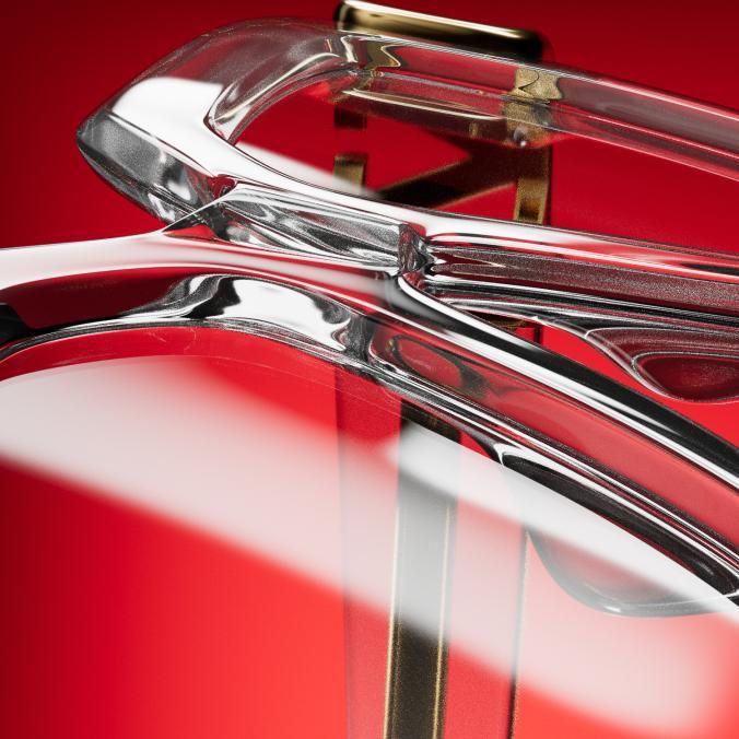 Close-up of a clear, glassy frame over gold metal details, against a red background with a soft streak of light.