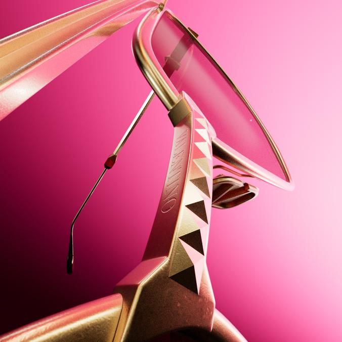 Close-up of a rose-gold temple lined with pyramid studs and engraved Valentino, holding a thin metal frame, against a pink background.