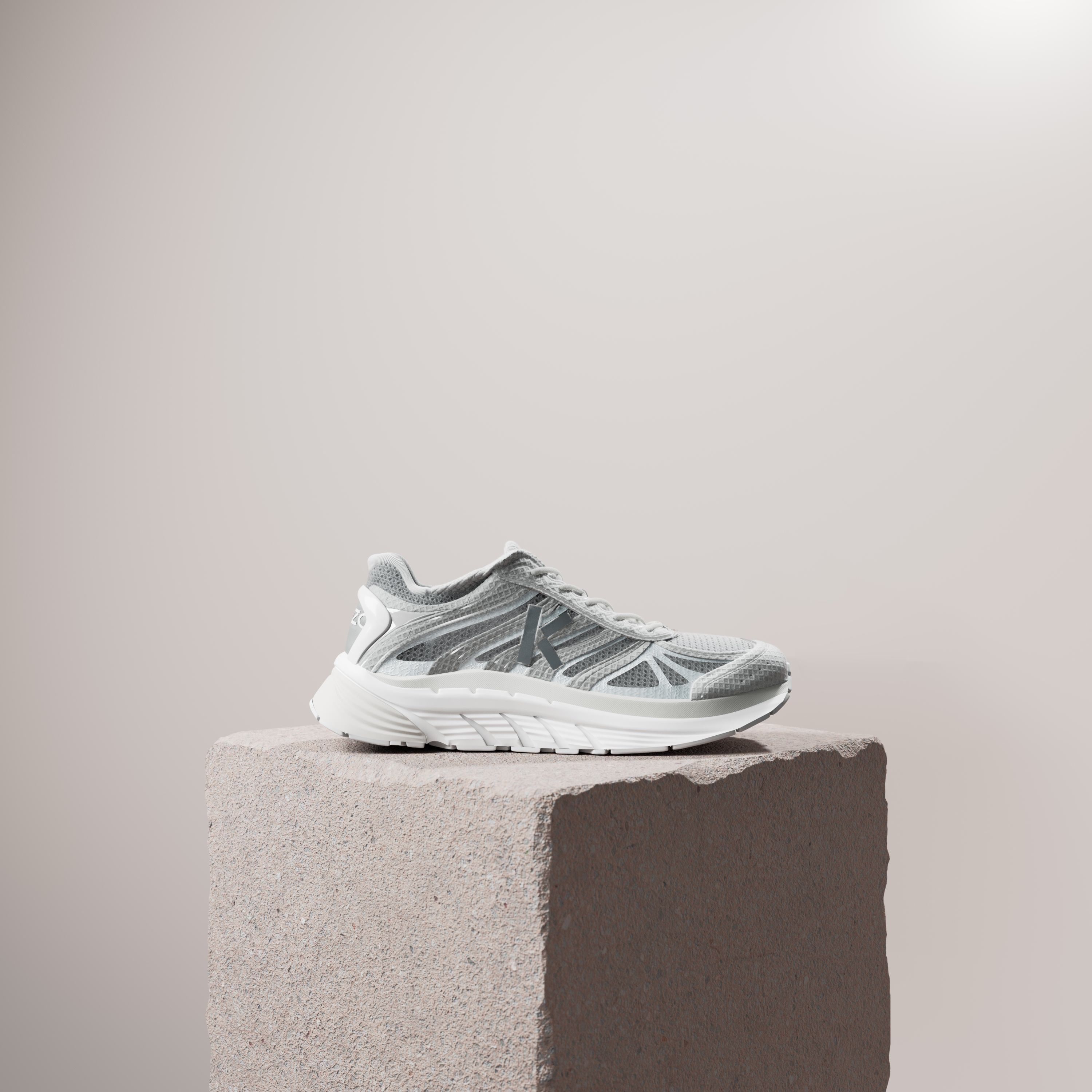 A silver and white running shoe on a rough stone plinth against a pale beige wall.