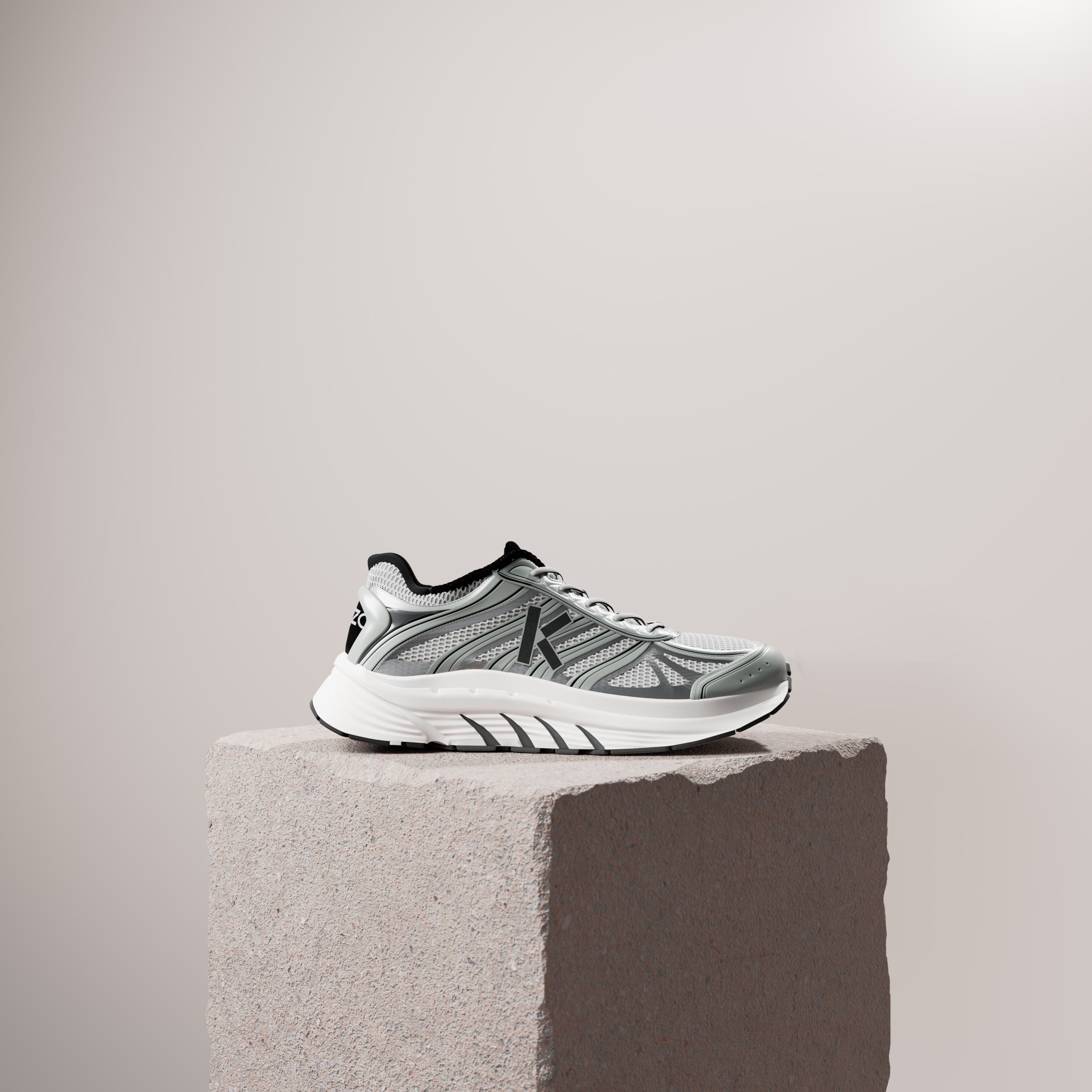 A white and grey running shoe with a black heel on a rough stone plinth against a pale beige wall.